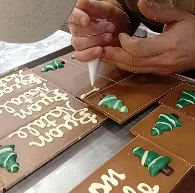 Le mani di chi scrive «Buon Natale» col cioccolato bianco su una tavoletta